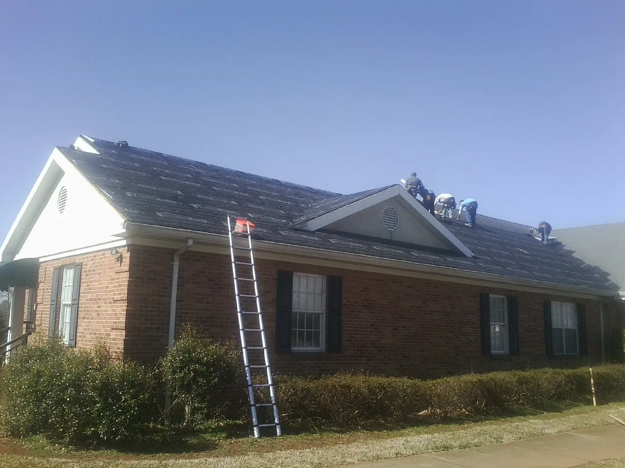 Crew tearing shingles off a brick ranch roof with a ladder set — Emergency Roof Repair work by our crew in Amboy
