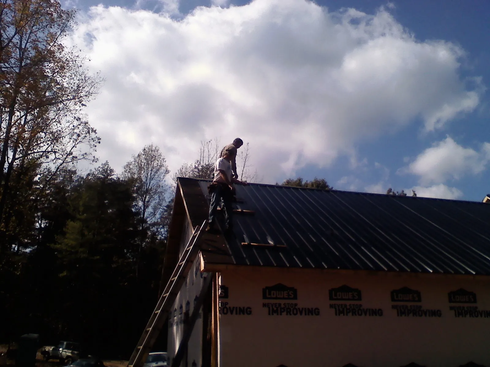 Roofer fastening dark metal panels high against a cloudy sky, from a Roof Inspection job in Amboy