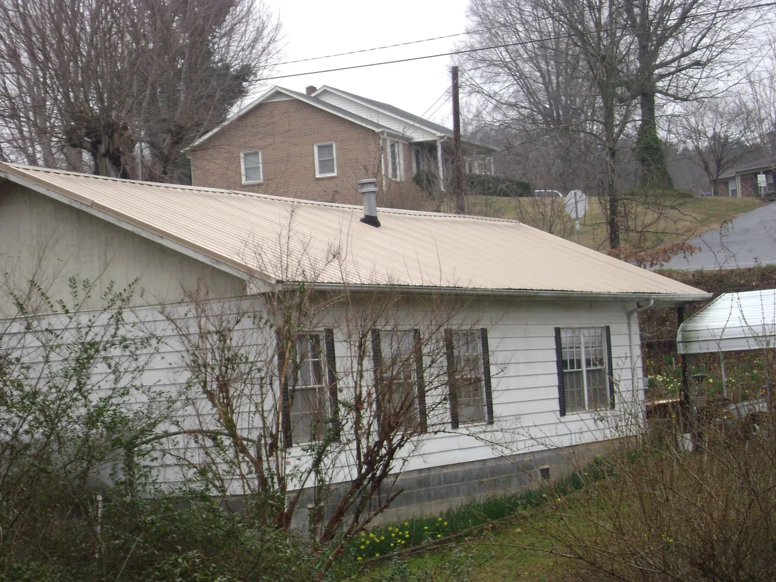 Tan metal roof on a white sided house set into a hillside — Commercial Roofing by Roofing Brothers in Amboy